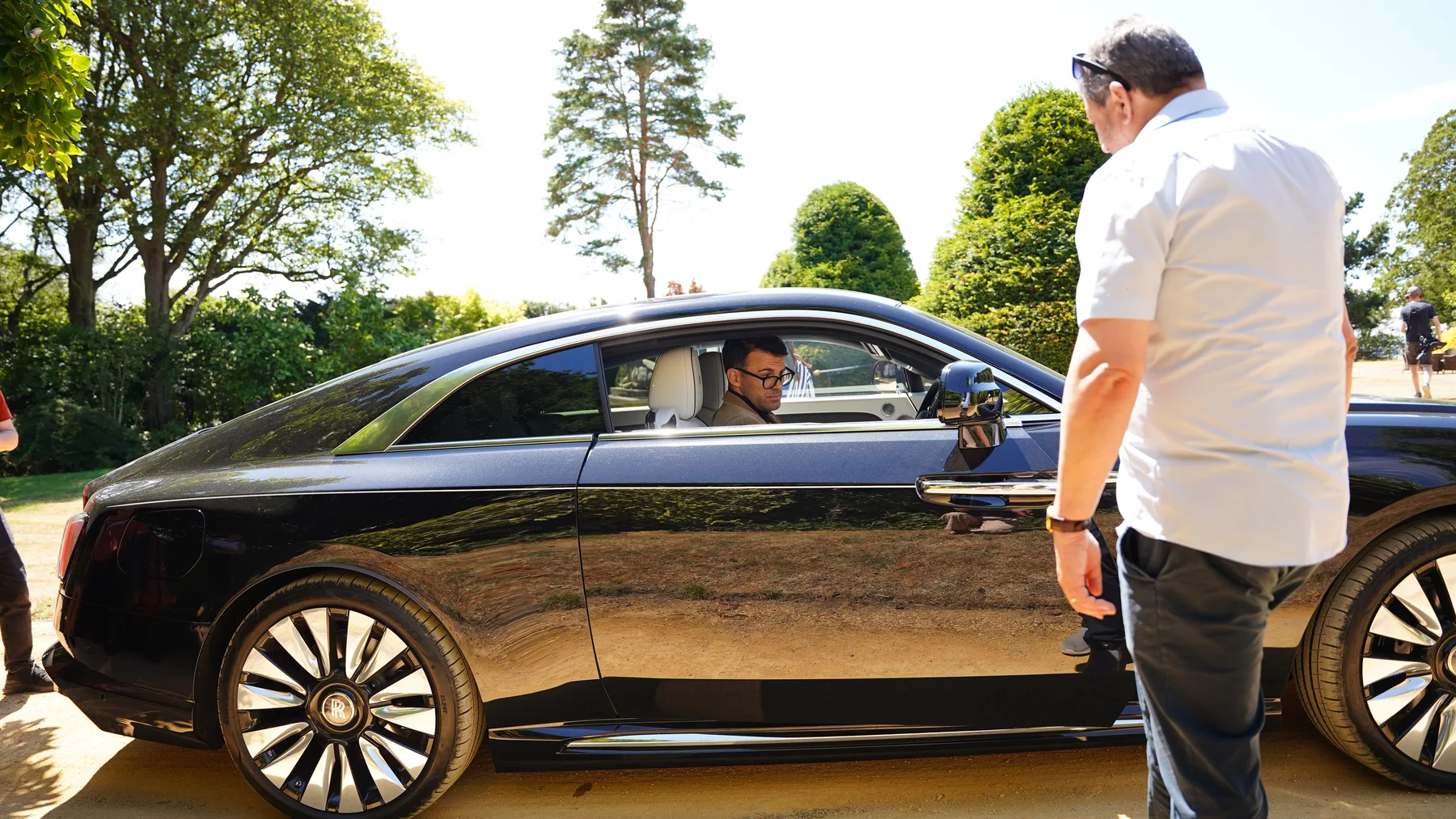 Cast and crew preparing a scene beside a black car