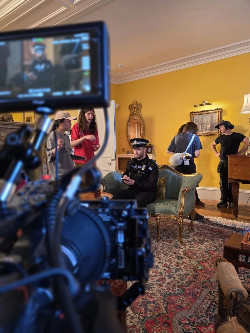 Camera and production monitor framing an actor in police uniform in the manor drawing room