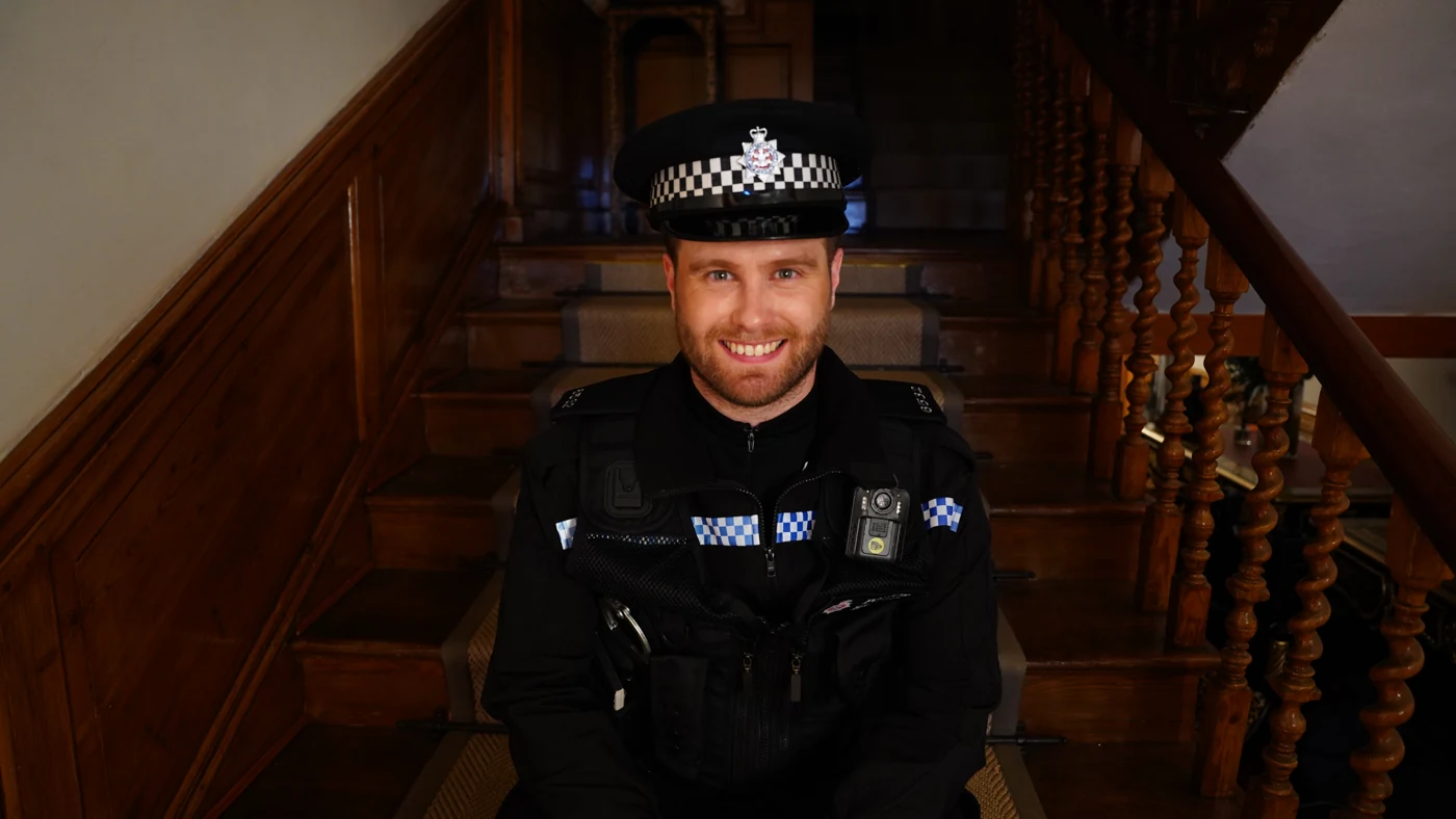 James Ellacott in a police costume seated on a staircase