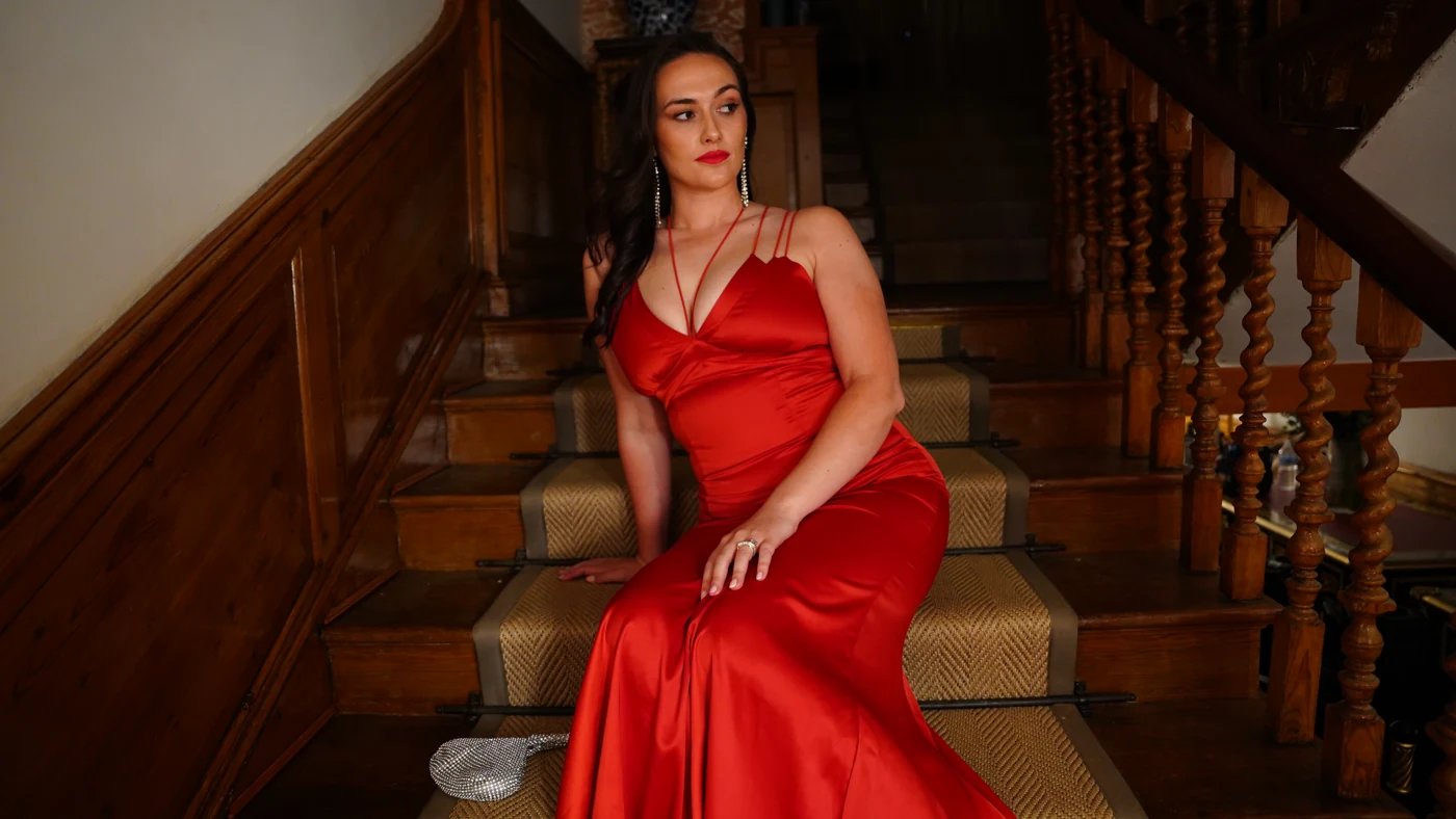 Tamara Brabon in a red dress seated on a staircase