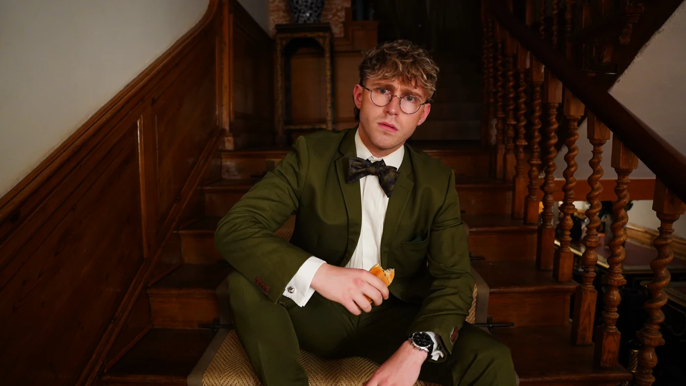 JJ Bennett in a green suit and glasses seated on a staircase