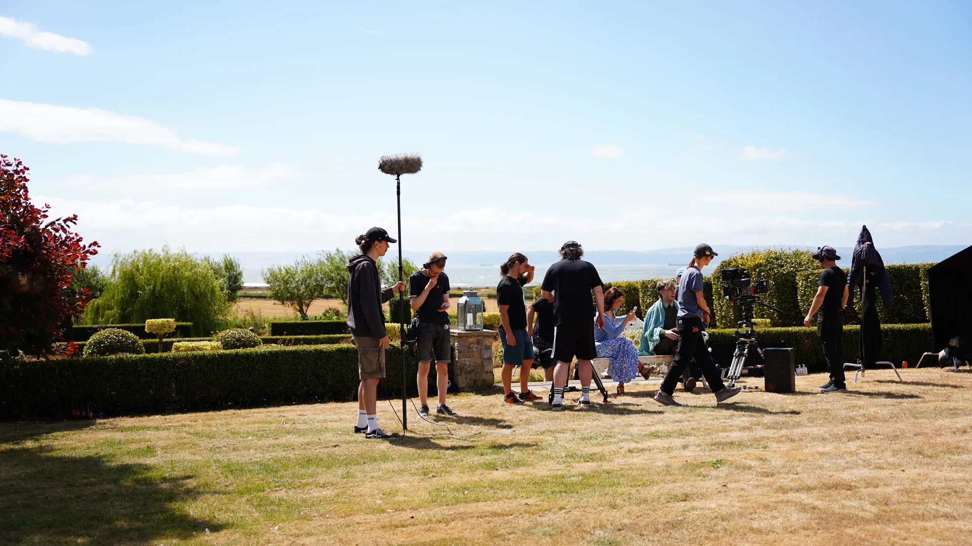 Cast and crew filming a garden scene with a boom microphone and camera